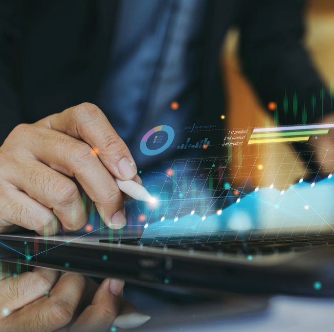 Imagem de uma mão masculina segurando uma caneta com superficie branca e apoiando a mão em cima de um notebook no qual, está saindo algumas ilustração de efeitos de luz, gráficos e dados.